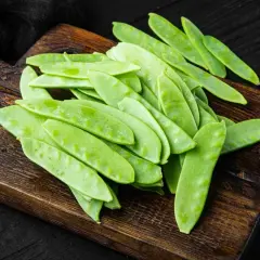 Un mucchio di taccole fresche, verdi e piatte, su un tagliere di legno scuro. Cosa sono? Deliziose!