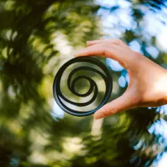 A hand holds a circular filter with a swirly bokeh pattern, creating a vortex of light and color.
