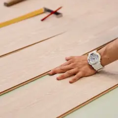 Mano con orologio bianco posata su pannelli di parquet chiaro, pronti per essere tagliati.