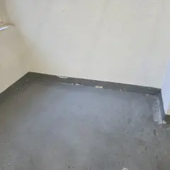 Ecke eines Raumes mit grauem Boden und weißer Wand. Der graue Sockelbereich zeigt Abplatzungen, ein Zeichen dafür, ab wann ist ein Keller feucht.