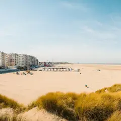 Breiter Sandstrand mit Dünen und Strandkörben in Belgien, Knokke. Lange Häuserzeile am Boulevard.