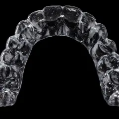 Przezroczysty aparat Invisalign, trzymany palcami, z widocznymi indywidualnymi nakładkami na zęby.