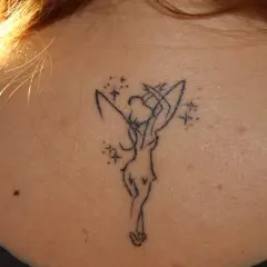 Delikatny tatuaż dzwoneczek z piotrusia pana na karku, otoczony magicznymi gwiazdkami.