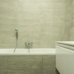 Salle de bain moderne avec baignoire blanche, carrelage gris clair et porte-serviettes chromé. Idéal pour apprendre comment rénover une baignoire.