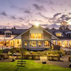 Abendstimmung am Golfclub Heckenhof. Beleuchtetes Clubhaus mit Terrassen und Gartenanlage im Dämmerlicht.