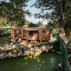 Une maison bioclimatique en bois, perchée près d'un étang verdoyant, entourée d'arbres majestueux.
