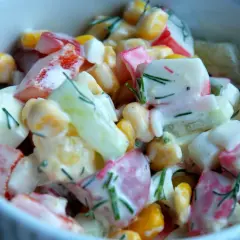 Pyszna sałatka z surimi, kukurydzy, ogórka i jajka, polana kremowym sosem i posypana koperkiem.