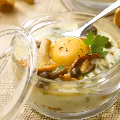 Un œuf au plat, entouré de champignons et de persil, dans un ramequin en verre. Un plat savoureux d'œufs au four.