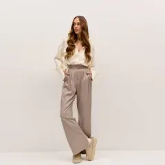 Młoda kobieta w eleganckim, beżowym zestawie: luźna koszula i szerokie spodnie.