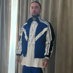 Malik Montana w niebieskiej kurtce i białej koszulce, gotowy na spotkanie z malik montana dzieci.