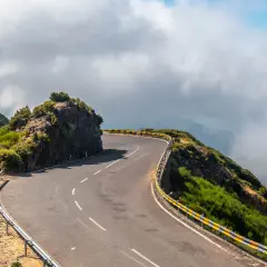Curva pronunciada en la **ruta N2 Portugal**, bordeada por barrancos y vegetación exuberante, con nubes bajas cubriendo el paisaje montañoso.