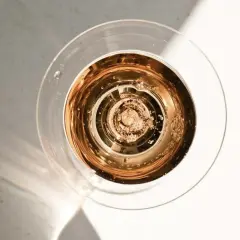 Szklanka z różowym, musującym winem dealkoholizowanym, w świetle słońca. Bąbelki unoszą się ku górze.