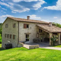 Belle ferme en pierre, résultat d'une rénovation réussie, nichée dans un paysage verdoyant sous un ciel bleu.
