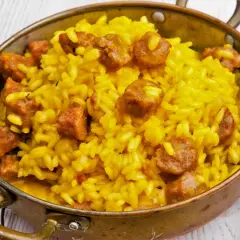 Arroz a la milanesa, un plato amarillo vibrante con trozos de salchicha, servido en un cuenco de cobre.