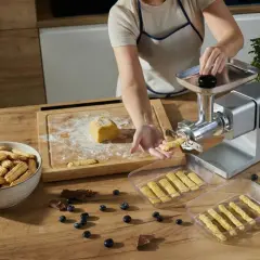 Przygotowanie pysznych ciastek wyciskanych z maszynki. Ciasto na desce, świeżo wyciśnięte ciasteczka w pojemnikach i misce.