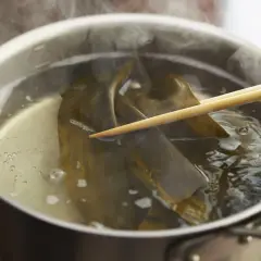 Kombu water steams in a pot as chopsticks gently hold the seaweed, infusing the broth with umami.
