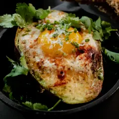 Un avocat oeuf au four, garni de coriandre fraîche et de ciboule, servi dans une poêle en fonte avec du pain grillé.