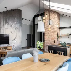 Nowoczesny styl loftowy salon z jadalnią i kuchnią. Ściana z motywem ważek, szara sofa, drewniany stół i ceglana ściana.