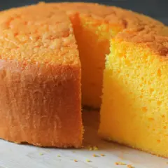 Puszysty, pomarańczowy tort z widocznym kawałkiem ciasta, gotowy do podania.