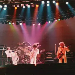 Zespół Electric Light Orchestra na scenie, grający największe przeboje. Kolorowe światła sceniczne podkreślają atmosferę koncertu.