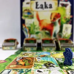 Gra planszowa "Łąka" w akcji. Drewniany pionek turysty na planszy pełnej kart z motywami przyrody.