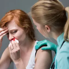Kobieta z krwawiącym nosem, trzymająca chusteczkę. Obok stoi osoba w rękawiczkach, która ją wspiera. Czy to objaw APTT?