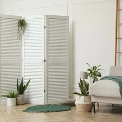 Weißer Klapp-Raumteiler mit Pflanzen und Sofa in hellem Wohnbereich.