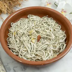 Un cuenco de barro con gulas al ajillo, ajo y guindilla. Un tenedor plateado a la izquierda y flores blancas al fondo.