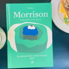 Zielona okładka książki Toni Morrison "Najbardziej niebieskie oko" leży obok filiżanki kawy i kanapki.