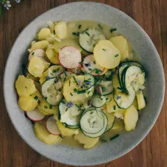 Ein Teller mit traditionellem bayrischem Kartoffelsalat, garniert mit Radieschen, Gurken und Schnittlauch.