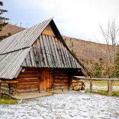 Drewniana chata w Dolinie Kościeliskiej, z widokiem na stoki górskie. Trasa turystyczna wczesną wiosną.