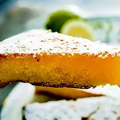 Una fetta di torta caprese al limone, spolverata di zucchero a velo, con fette di limone sullo sfondo.