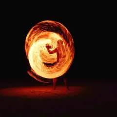 A performer creates a fiery vortex with a poi in this stunning fire photography. The flames swirl around them, illuminating the dark night.