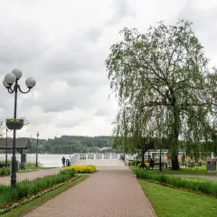 Spacer w Mrągowie nad jeziorem, z wierzbą płaczącą i kwitnącymi rabatami. To jedne z wielu mrągowo atrakcje.