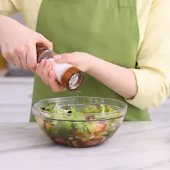Manos sazonando una ensalada con sal, uno de los usos de la sal en la cocina.