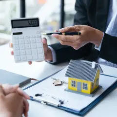 Conseiller montrant un calcul sur une calculatrice pour une aide premier achat immobilier. Une maison miniature et des clés sont sur un contrat.