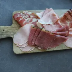 Holzbrett mit verschiedenen Aufschnittsorten, darunter zarter **prosciutto crudo**, Schinken und Rindfleisch.