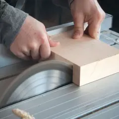 Mani esperte guidano un pezzo di legno su una sega circolare, uno degli attrezzi per tagliare il legno con precisione, per creare un taglio netto.
