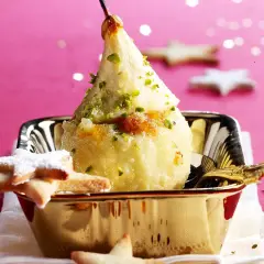 Poire pochée, garnie de pistaches et de miettes de biscuit, servie dans un bol doré. Une idée gourmande pour une recette chartreuse.