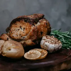 Un délicieux roti de veau, rôti à la perfection, accompagné de pommes de terre, d'ail, de romarin et de rondelles de citron sur une planche en bois.