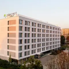 Nowoczesny hotel Element by Westin z zielonym logo na dachu, otoczony drzewami i innymi budynkami.