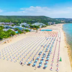 Słoneczna plaża w Bułgarii z rzędami leżaków i parasoli. W tle hotele i zielone wzgórza. Ceny w Bułgarii zachęcają do wypoczynku.