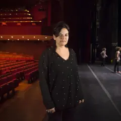 Emma Dante in un teatro, con le poltrone rosse vuote e il palco illuminato.