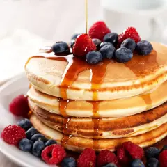 Pancake ricetta: una pila di soffici pancake guarniti con sciroppo d'acero, lamponi e mirtilli freschi.