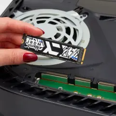 Dłoń z czerwonym lakierem trzyma dysk SSD M.2 PCIe 4.0 NVMe, gotowy do montażu w konsoli.