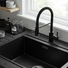 Nowoczesna kuchnia z czarnymi zlewozmywakami i elegancką baterią. Obok stoją szklanki i butelki.
