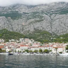 Widok na miasto Makarska z górami w tle. W porcie cumują liczne łodzie i jachty. Choć nie ma tu lotniska, widok zapiera dech w piersiach.