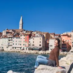 Frau sitzt auf Felsen mit Blick auf die Küstenstadt Rovinj in Kroatien.