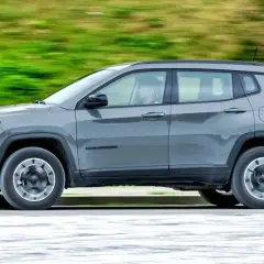 Szary Jeep Compass 4xe w ruchu, z rozmytym zielonym tłem.