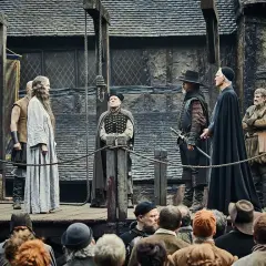 Grupa ludzi na platformie, w tym kobieta w jasnej sukni, mężczyźni w strojach z epoki i żołnierze. Atmosfera sugeruje spisek prochowy i jego konsekwencje.